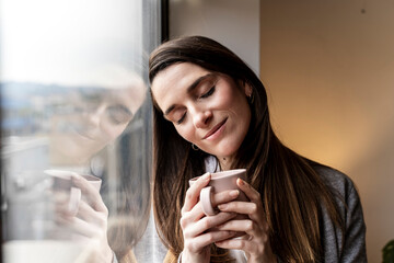 Woman with long hair holding a coffee cup by a window with reflection