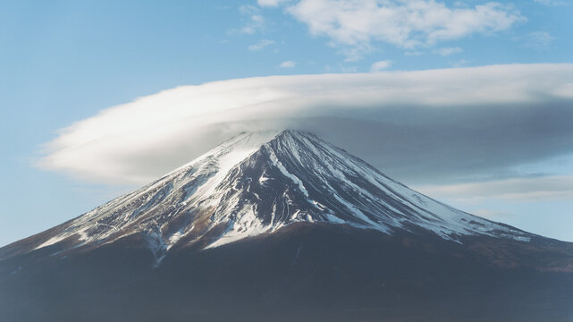 View of the majestic Mount Fuji peak capped with a striking lenticular cloud, standing tall against the clear blue sky, Fujikawaguchiko, Yamanashi, Japan.