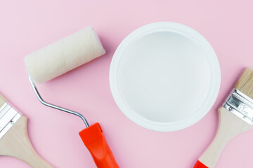 Painting supplies with brushes and roller on pink background for DIY and interior decor concept