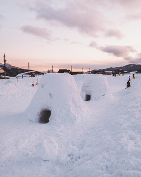 View of snow-covered igloos stand nestled in the pristine white landscape beneath the soft hues of the sky, creating a serene winter scene, Iiyama, Nagano, Japan.