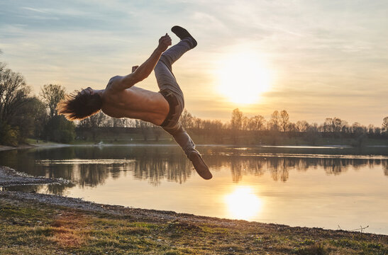 Germany, Bavaria, Feldkirchen, man doing parkour at lakeshore