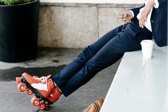 Businesswoman wearing roller skates, drinking coffee and using smartphone