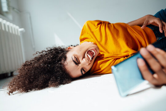 Angry woman shouting while holding mobile phone on floor