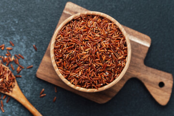 Red rice in wooden bowl on cutting board with scattered grains and spoon
