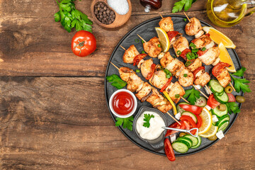 Top view of grilled chicken skewers with vegetables, sauces, and fresh salad on a rustic wooden table setting. top view. copy space