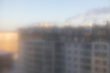 Window with a blurry view of a building. The window is foggy and the building is tall