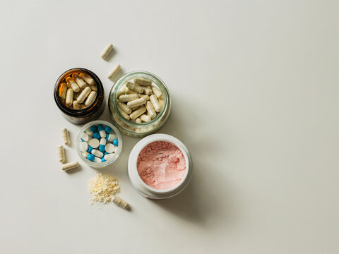 Top view of assorted health supplements including pills, capsules and colorful powders on clean white background flat lay