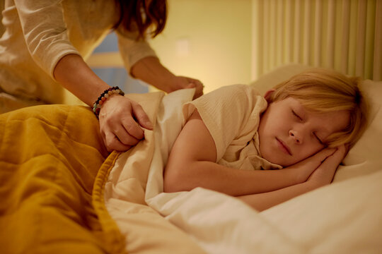 Mother tucking in her son at night in a cozy bedroom