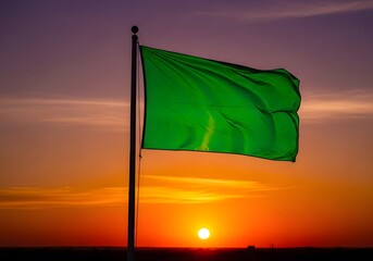 Vibrant green flag on a flagpole waving against a dramatic sunset sky