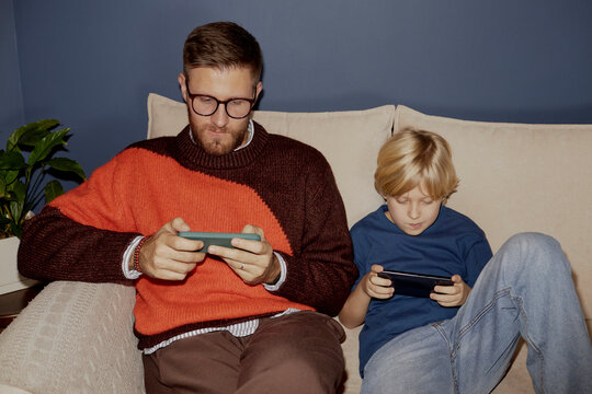 Father and son bonding at home using smartphones on the couch