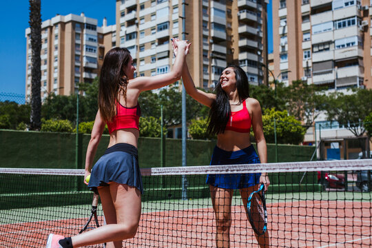 Two happy female tennis players high fiving at the net