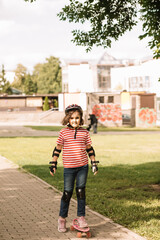 Cute kid girl child riding a skateboard in skatepark. Child performs tricks. Summer sport activity concept. Happy childhood.