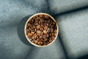 Coffee beans in wooden bowl with shadow on dark background