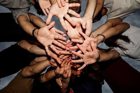 Group of friends stacking hands against sky in park at sunset