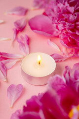 Pink peonies and petals with a burning candle on pastel pink background