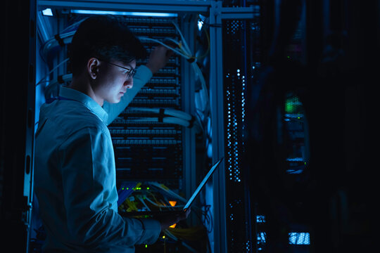 Computer engineer is setting up network in server room,Systems Maintenance Technician,Male engineer working in server room at modern data center