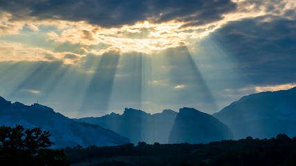 Sunbeams breaking through clouds over blue mountain range