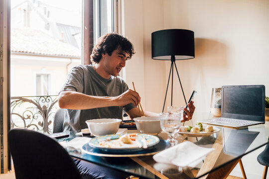Man using mobile phone while having lunch at home