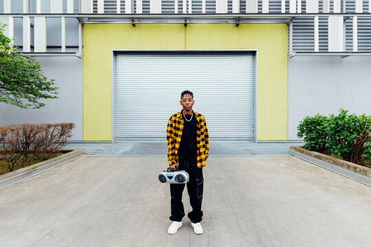 Young man holding boom box standing in front of shutter
