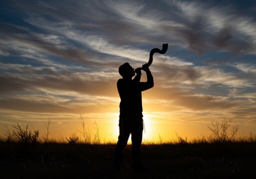 Silhouette of a man blowing a shofar against a vibrant sunset sky