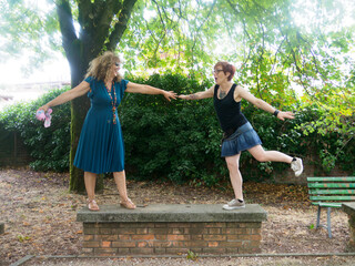 Naklejka premium Two Women Holding Hands Standing on a Brick Platform in a Park Enjoying a Sunny Day Together