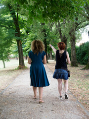 Two Women Walking on a Gravel Path Under a Canopy of Lush Green Trees on a Sunny Day Enjoying the...