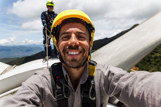 Engineer taking a selfie on a wind turbine nacelle with a colleague in the background
