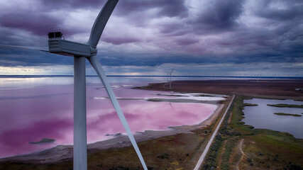 Aerial view of the striking contrast of the pink Lemurian Lake against the moody sky, with wind turbines standing tall, Lemurian Lake, Kherson Oblast, Ukraine.