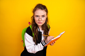 Focused student taking notes with a determined expression on her face against a vibrant yellow background