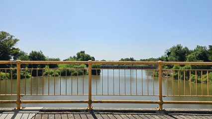 Rusty Yellow Bridge Railing over Calm River on Sunny Day