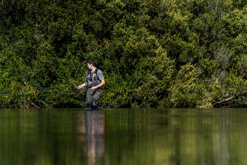 Man fly fishing in a crystal-clear mountain river, surrounded by nature. Peaceful landscape, wilderness adventure, and passion for the outdoors.