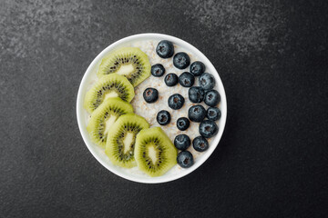 Healthy breakfast bowl with kiwi slices and blueberries on dark background