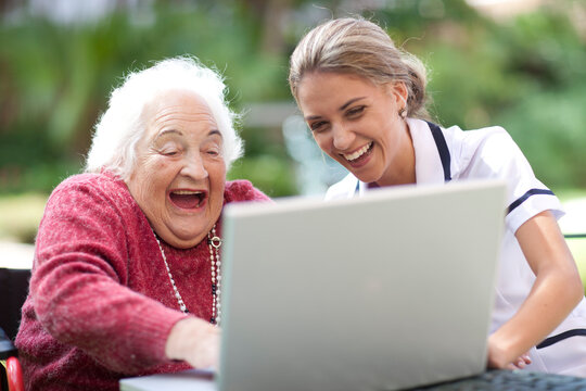 Happy nurse and senior woman using laptop together