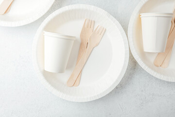 Scattered white paper cups and wooden forks on white disposable plates
