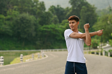 A Fit young Asian man preparing for a run, stretching muscles outdoors on a scenic road