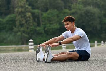 An Asian Male athlete in sportswear stretching legs before jogging, showing flexibility and proper...