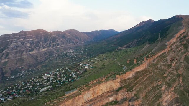 Aerial view of Goor village nestled on a lush, green mountainside with winding dirt roads and ancient stone towers, creating a striking contrast, Goor, Republic of Dagestan, Russia.