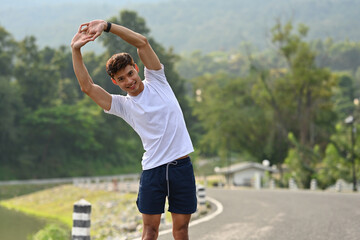 A smiling man doing side bends during warm-up on a road, emphasizing flexibility and active living