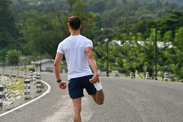 Back view of a man stretching his leg muscles before running on a road, promoting fitness, exercise, and healthy lifestyle concepts
