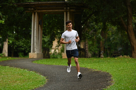 An Asian Athletic man jogging on a scenic park trail surrounded by greenery, promoting a healthy lifestyle and outdoor fitness