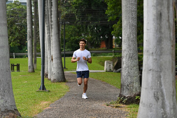 An Asian man jogging on a scenic park trail lined with tall trees, enjoying outdoor exercise and fitness in nature