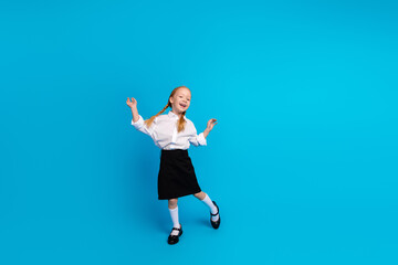 A joyful young schoolgirl in uniform smiling confidently against a bright blue background...