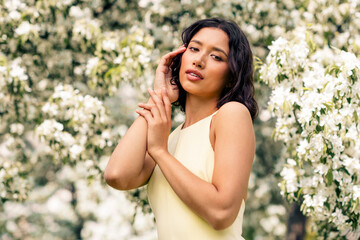 Beautiful young woman in yellow dress enjoying nature surrounded by blooming flowers on a bright...