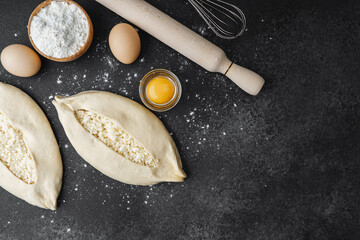Two raw khachapuri breads on black floured table with baking ingredients