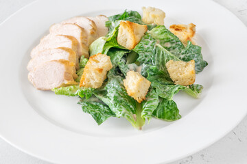 Classic Caesar salad topped with chicken breast served on clean white plate