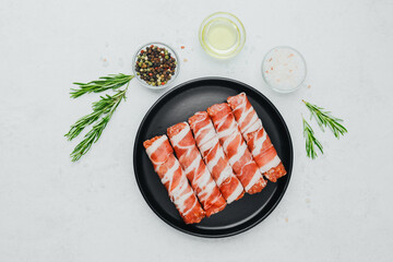 Bacon wrapped sausages on black plate with spices and rosemary