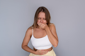 Young blonde woman holding her stomach and covering her mouth with discomfort experiencing nausea...
