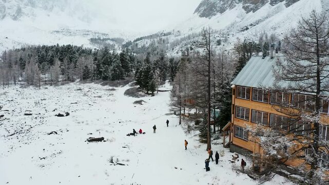 Aerial view of a snowy landscape with mountains, trees, and a small settlement, a group of people stand near a fire, Aktau, Republic of Bashkortostan, Russia.