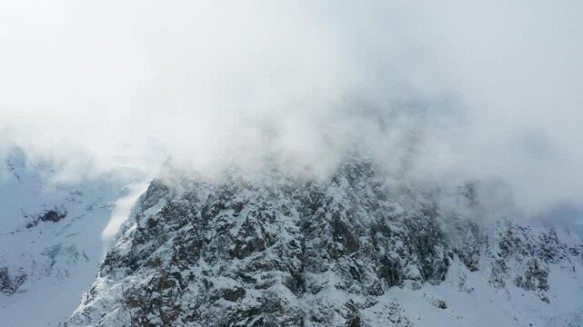 Aerial view of snow-laden mountains piercing through the heavy clouds, creating a striking contrast of white and grey, Aktau, Republic of Bashkortostan, Russia.