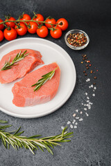 Raw veal steaks on white ceramic plate with tomatoes herbs salt oil and pepper